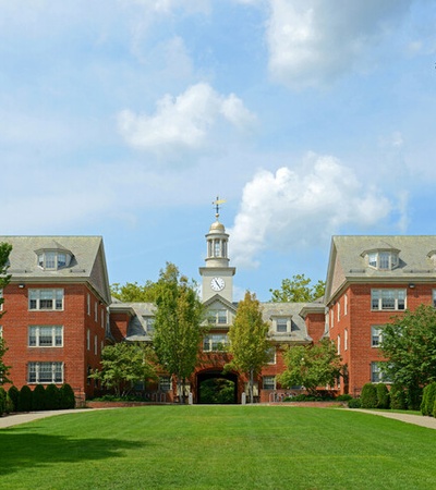 A scenic view of a college campus featuring brick buildings and a clock tower surrounded by greenery.