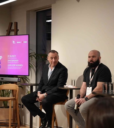 A panel discussion taking place in a modern setting with three men and a large screen displaying information.